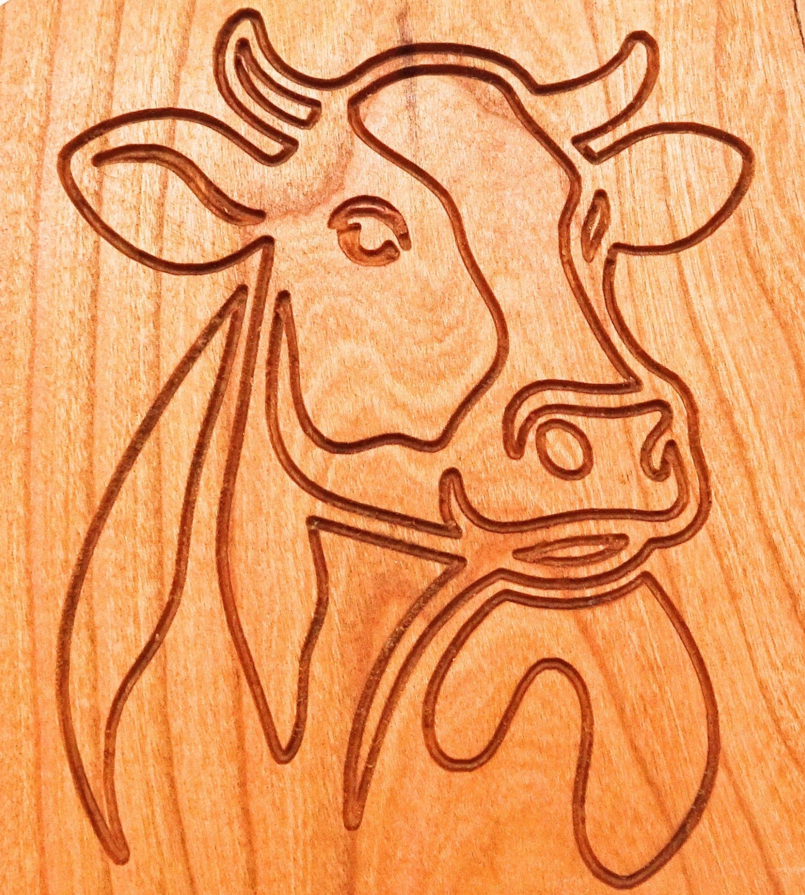 Cherry Wooden coaster  with a carved outline of a cow's head.